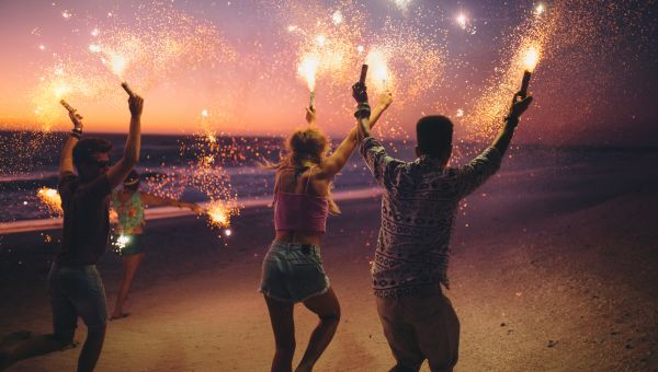 a group of young adults run across a beach carrying sparklers