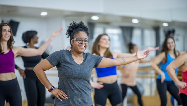 a smiling Black woman in workout wear strikes a pose in a group fitness class