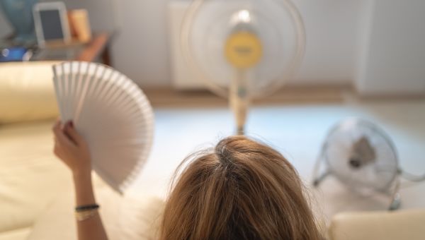 back view of a person sitting on a couch with a hand fan and two mechanical fans in front of them