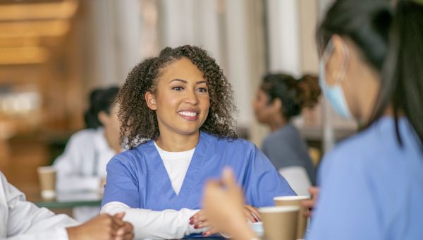 several nurses sit around a table at the cafeteria during lunch enjoying a conversation