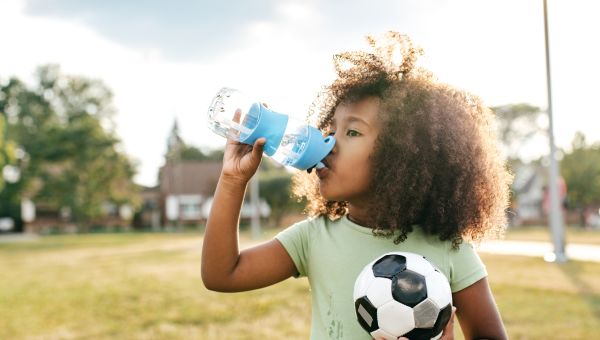 young girl drinking from water bottle and holding soccer ball