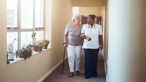 Elderly woman and caregiver walking down hallway.