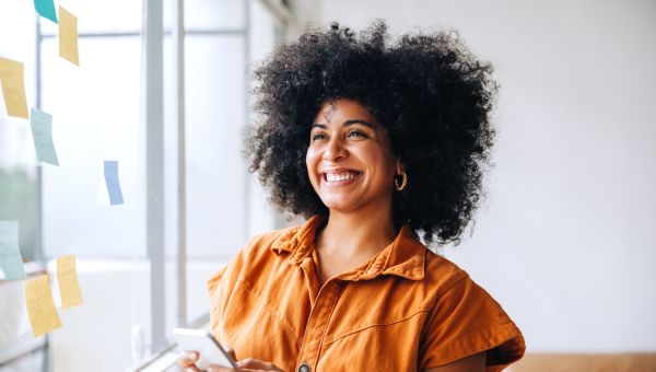 a young Black woman stands near a sunny window and smiles