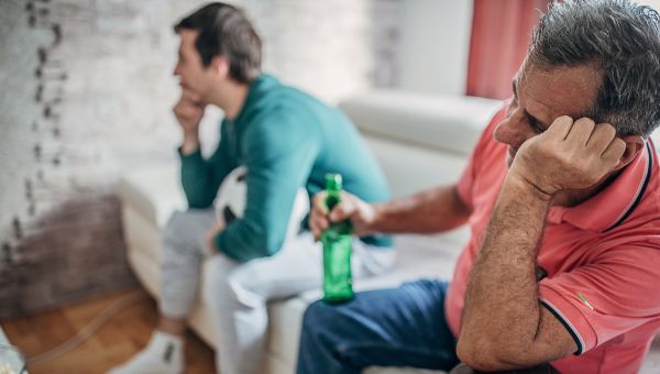 father and adult son watching tv while drinking beer