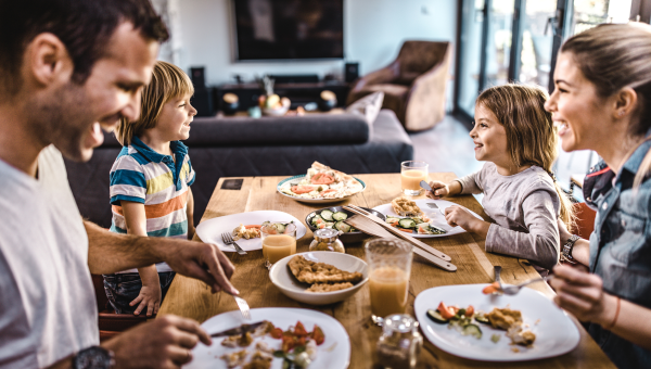 family of two parents and a boy and girl sit around the dinner table eating and laughing