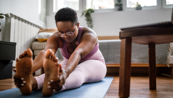 woman in her studio apartment stretches in a yoga pose on a mat on the floor