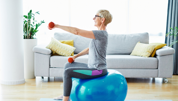 senior woman sitting on balancing ball lifting light weights