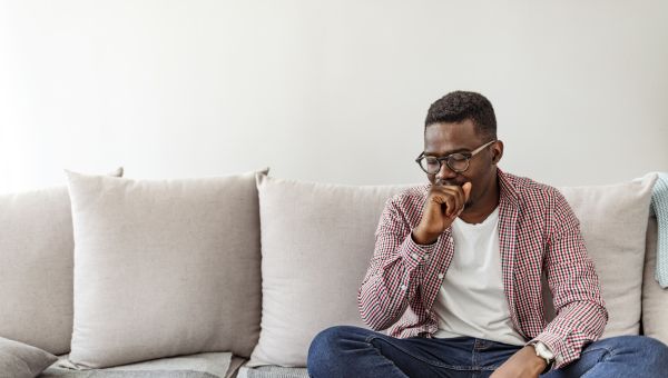 man on his couch coughing