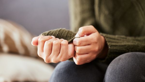 closeup of a worried woman sitting on the couch, her hands tugging on her sweater