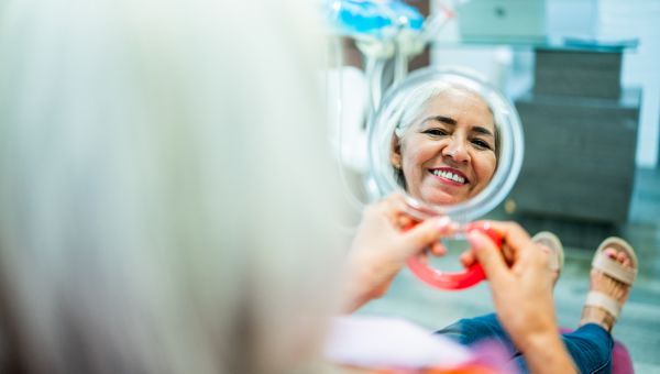 senior woman smiling in the mirror in the dental office after a whitening treatment