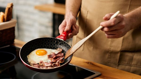 man cooking eggs and turkey bacon in a skillet