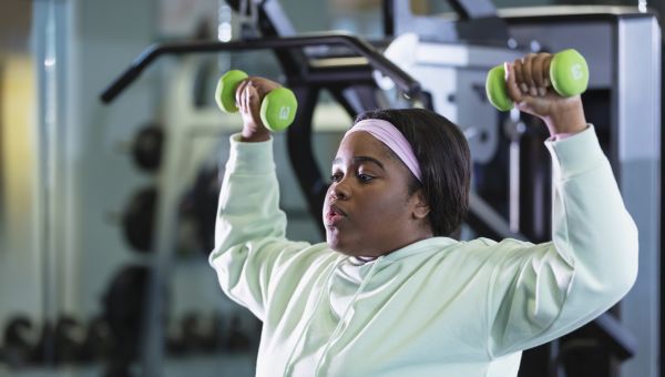 a young Black woman does shoulder press exercises with light dummbells