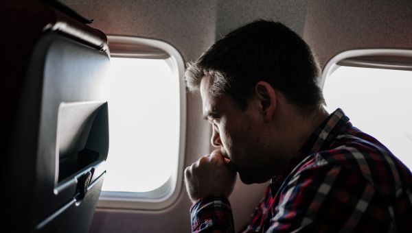 side view of a man coughing in his seat on a plane