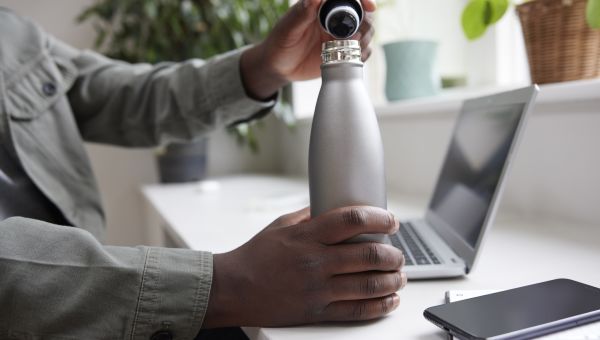 man taking cap off water bottle at desk