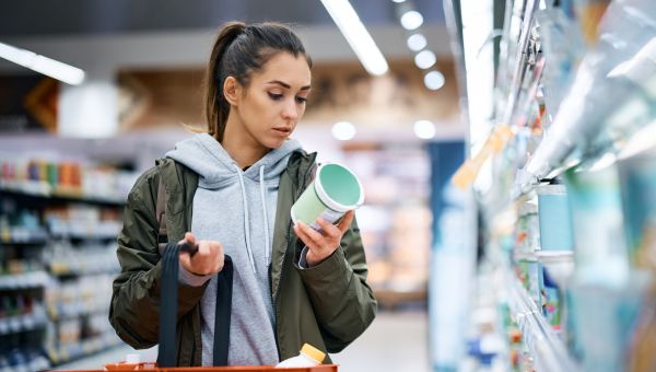 woman reading ingredients on a container of food in grocery store