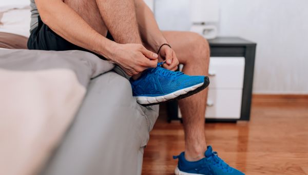 man sitting on bed lacing up running shoes