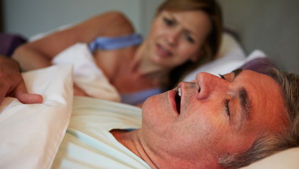 annoyed woman in bed with her husband who is talking in his sleep