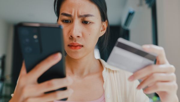 upset woman looking at phone with credit card