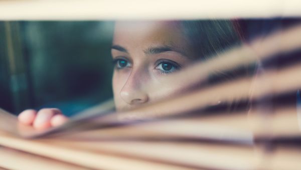 a woman with trauma looking through window blinds