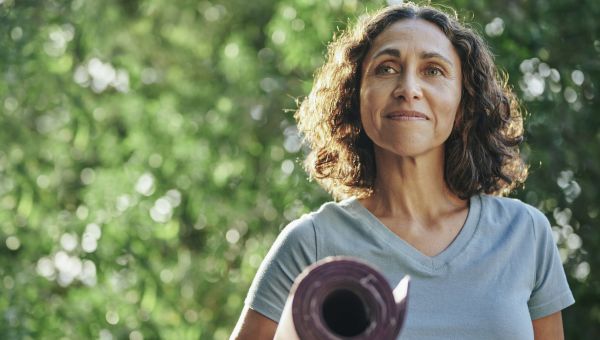 mature woman carrying yoga mat outdoors