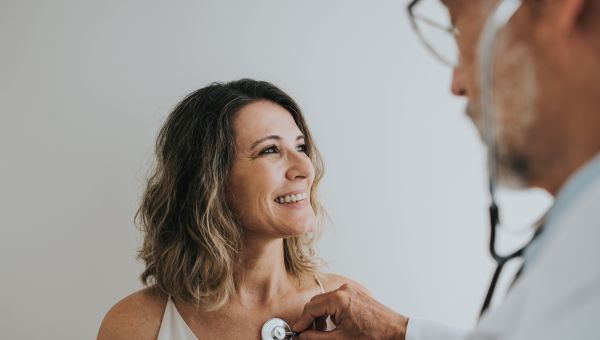 a middle aged latina woman has a checkup from a doctor who holds a stethoscope over her heart