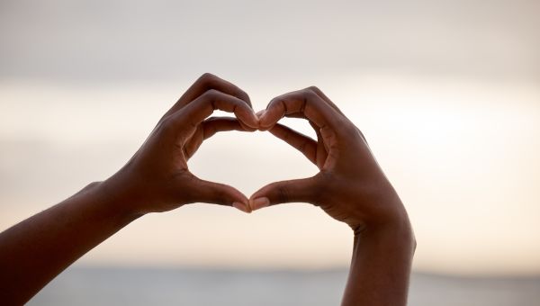 someone making a heart with their hands with the ocean in the background