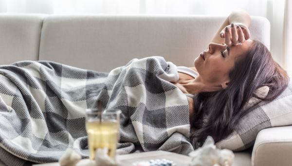 adult woman sick with the flu lying on a sofa under a blanket