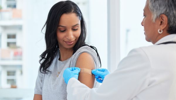 a young Black woman receives a bandage from her healthcare provider after receiving a vaccination