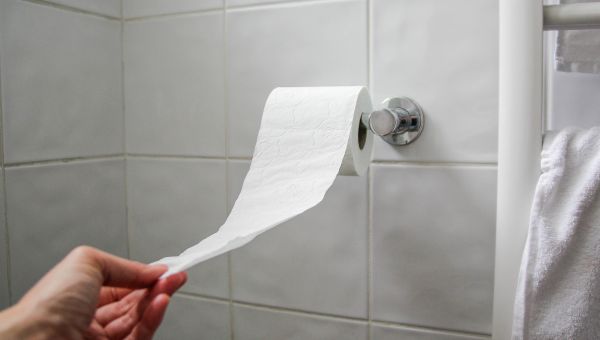 Someone reaching for a roll of toilet paper in the bathroom