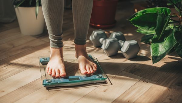 closeup image of a woman's feet and lower ankles standing on a glass digital scale, measuring her weight as part of her efforts to maintain a healthy weight and reduce the risk of breast cancer