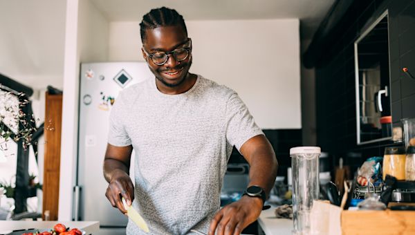 young man wearing eyeglasses and preparing fruit salad in home kitchen