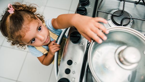 young girl reaching for boiling pot on stove