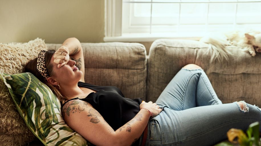 Middle aged woman with tattoos lying on couch in pain