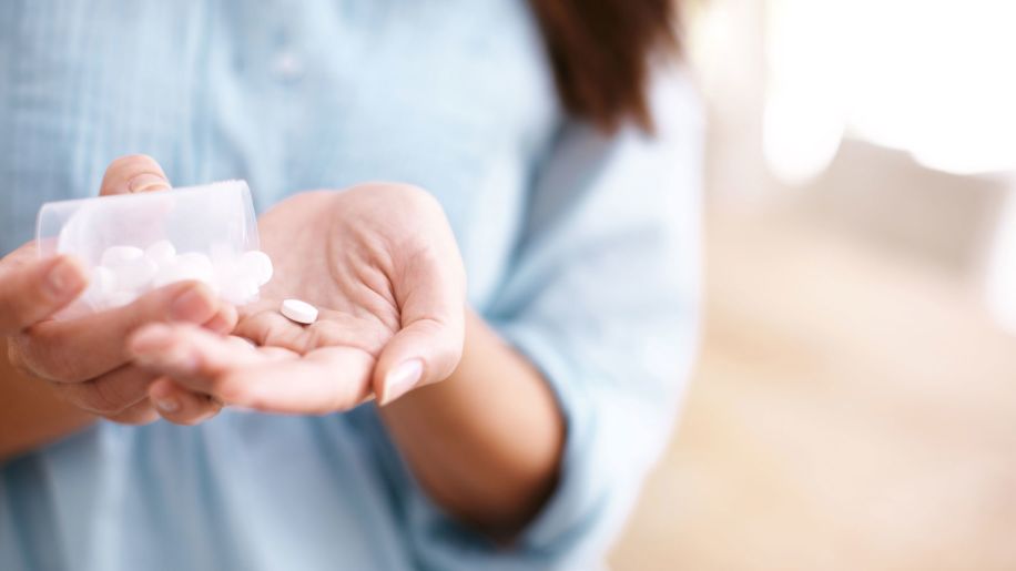 Woman tipping a bottle over to put a little white pill in her hand.