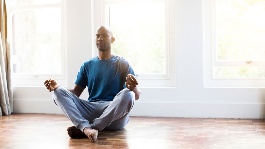 Man meditating in an empty room with plenty of windows.