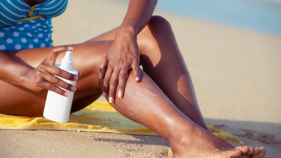 A woman at the beach putting sunscreen on her legs.