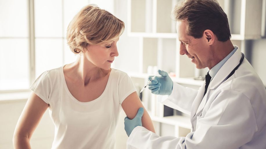 Middle-aged woman gets a needle in her arm administered by male doctor.