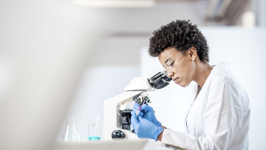 a young Black medical researcher looks into a microscope as part of her research