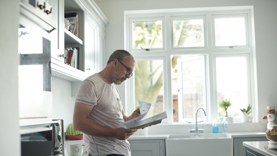 man reading through bills in his kitchen
