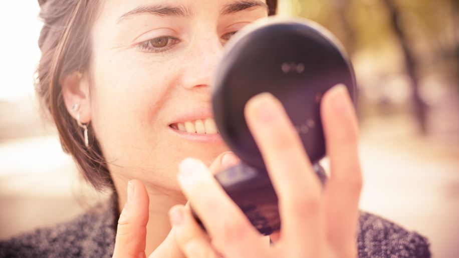 Woman applying makeup in compact mirror