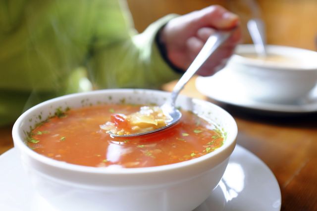 Bowl of hot vegetable soup and hand holding spoon.