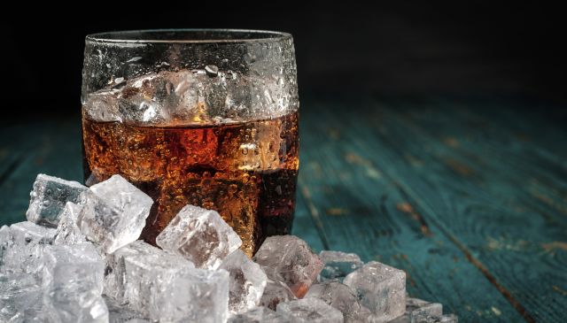 Glass of cola with ice on a wooden table. Copyspace on the right.