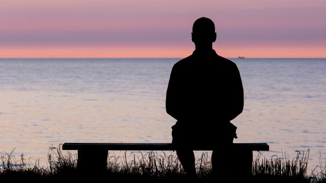 man sitting on bench staring out at seas, sunset
