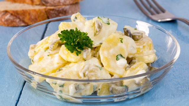 Potato salad in a glass bowl on wooden board.