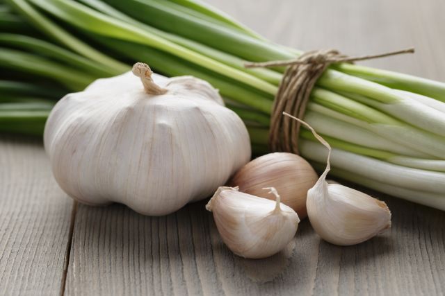 Bulbs of garlic, which may help with inflammation, heart health and more, sit on a wooden surface next to scallions