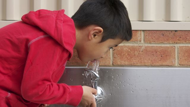 young latin boy drinks water out of a fountain, bubbler