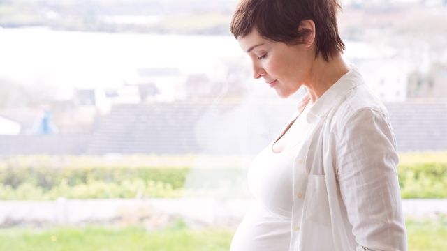 Older pregnant woman smiles as she looks down at her belly. 