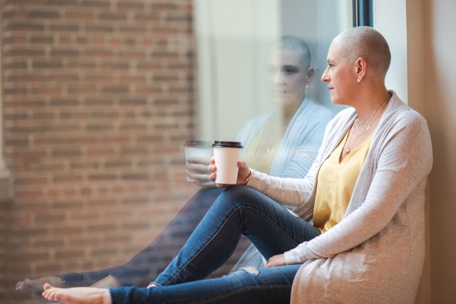 A female cancer patient enjoys coffee while looking out a window. Her treatment is going well.