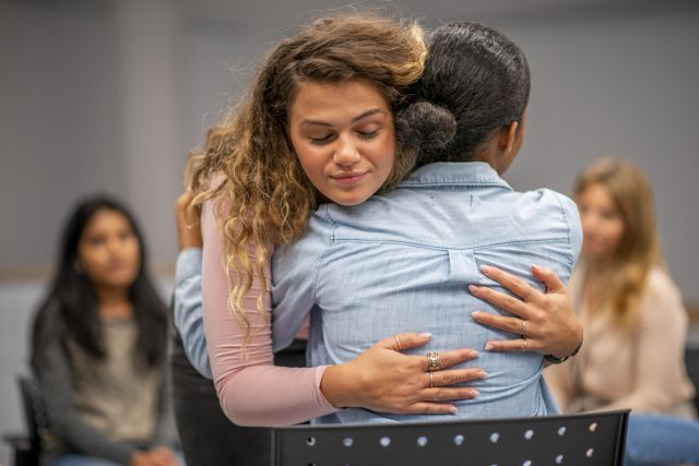 Two women embrace at a support group meeting. Support groups can help people cope with conditions like endometriosis.