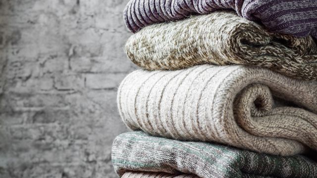 a stack of weighted blankets made of various types of fabric sits in front of a brick wall